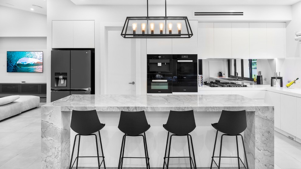 This is an example of a contemporary open plan kitchen in Sydney with flat-panel cabinets, mirror splashback, black appliances, with island, grey floor and grey benchtop.