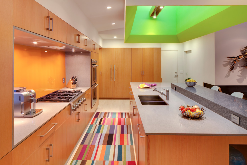 Design ideas for a modern galley kitchen in Los Angeles with a double-bowl sink, flat-panel cabinets, medium wood cabinets and orange splashback.