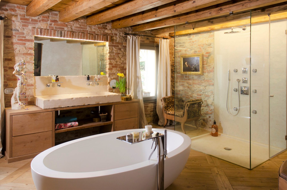 Photo of an eclectic master bathroom in Venice with flat-panel cabinets, light wood cabinets, a freestanding tub, a curbless shower, medium hardwood floors, a vessel sink, wood benchtops, a hinged shower door, a single vanity, a freestanding vanity, exposed beam and brick walls.