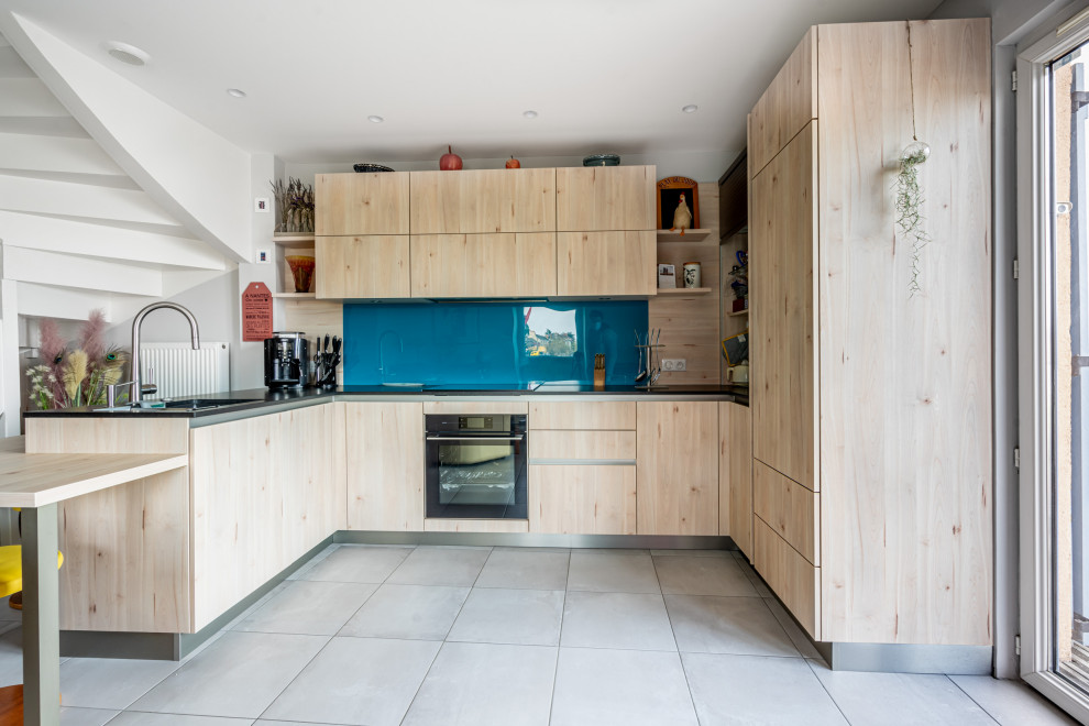 Photo of a large contemporary u-shaped open plan kitchen in Nantes with a submerged sink, flat-panel cabinets, light wood cabinets, granite worktops, blue splashback, integrated appliances, ceramic flooring, no island, grey floors and black worktops.