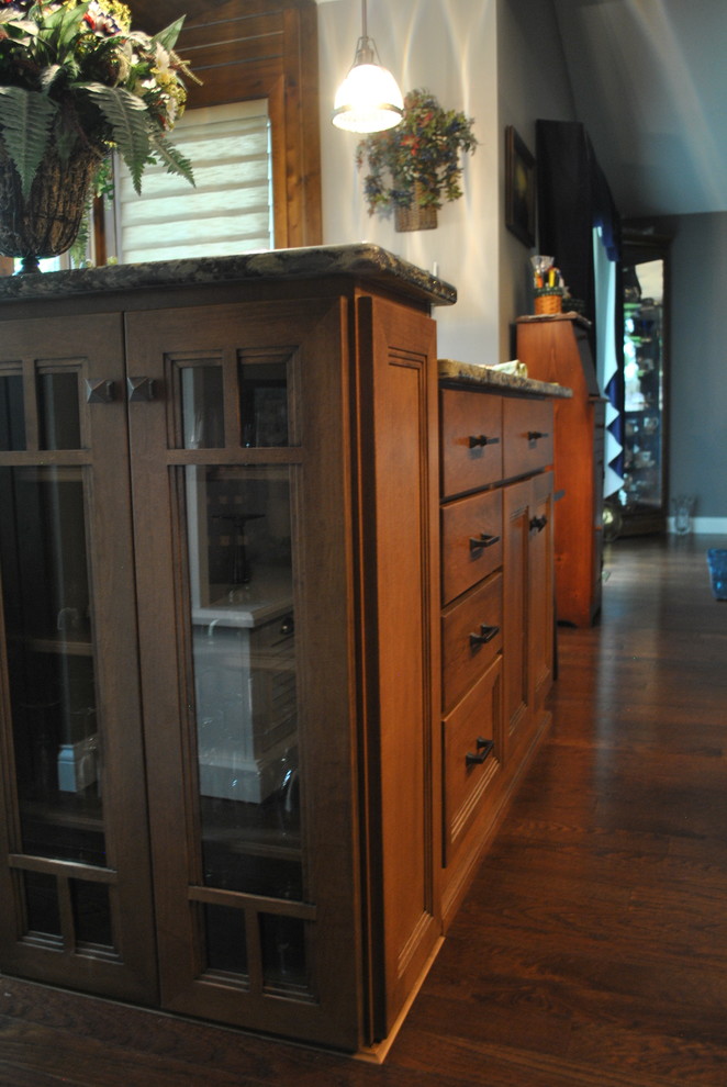 Example of a brown floor kitchen design with brown cabinets, beige backsplash, stainless steel appliances, an island and gray countertops