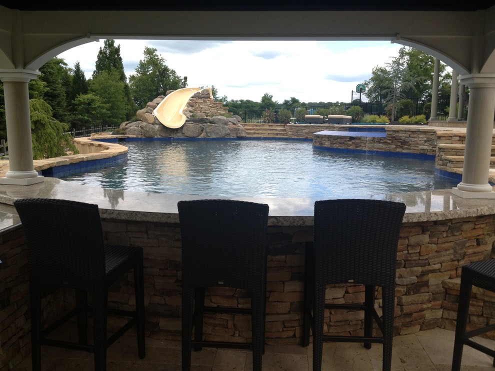 Large country backyard custom-shaped pool in Philadelphia with a water slide and natural stone pavers.