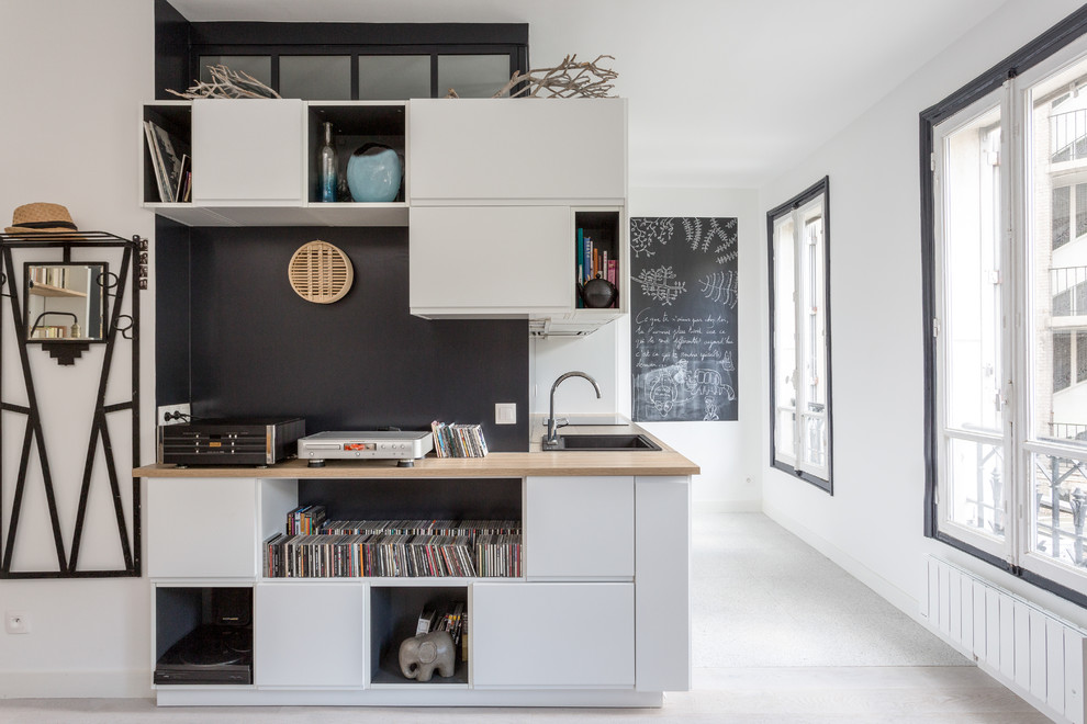 Photo of a mid-sized modern single-wall open plan kitchen in Paris with wood benchtops, a drop-in sink, flat-panel cabinets, white cabinets, black splashback, slate splashback, black appliances, vinyl floors, no island, grey floor and beige benchtop.