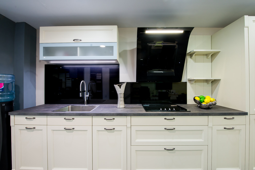 This is an example of a country single-wall open plan kitchen in London with a single-bowl sink, shaker cabinets, beige cabinets, laminate benchtops, metallic splashback, glass sheet splashback and black appliances.