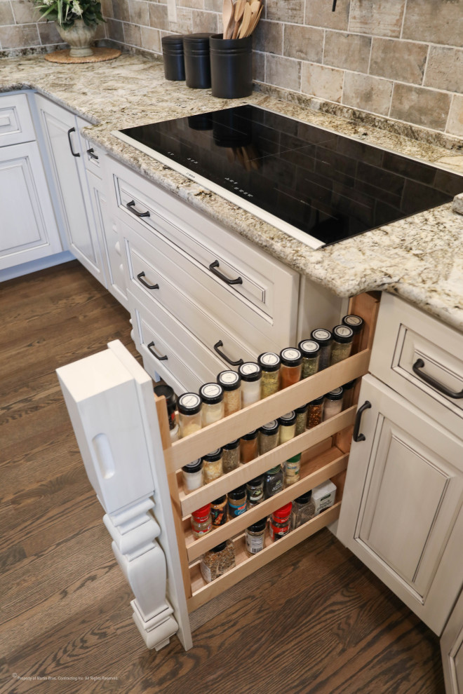 Inspiration for a large timeless u-shaped medium tone wood floor kitchen pantry remodel in Other with an undermount sink, raised-panel cabinets, white cabinets, granite countertops, porcelain backsplash, stainless steel appliances and an island