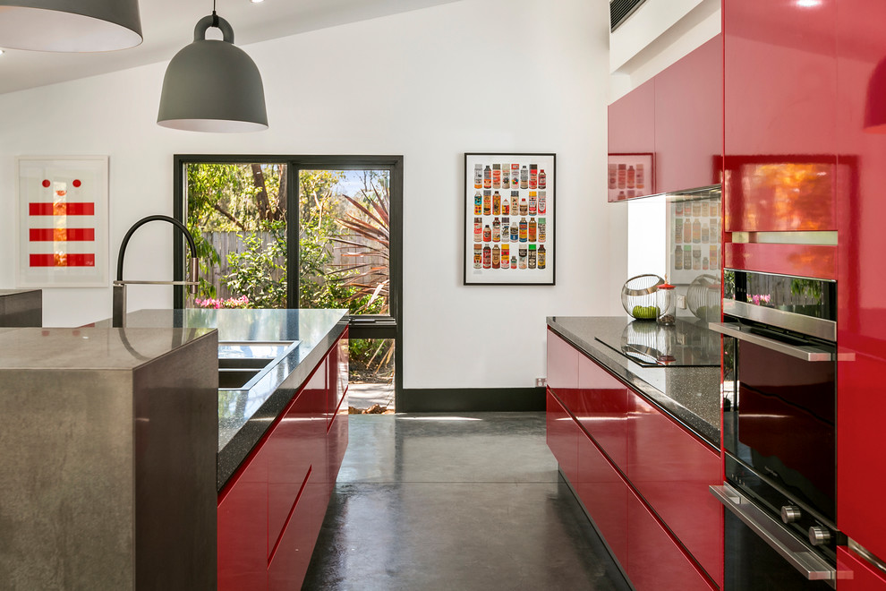 Photo of a contemporary galley kitchen in Sydney with a double-bowl sink, flat-panel cabinets, red cabinets, grey splashback, concrete floors, with island, grey floor and grey benchtop.