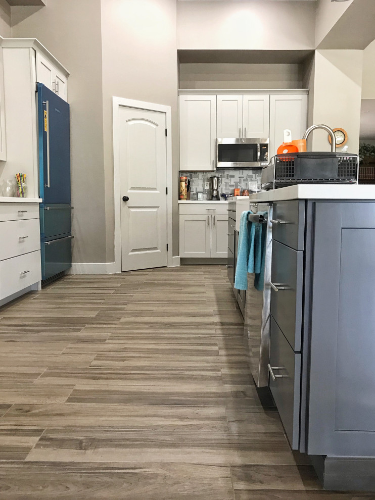 Mid-sized transitional l-shaped open plan kitchen in Phoenix with an undermount sink, shaker cabinets, white cabinets, quartz benchtops, white splashback, glass sheet splashback, stainless steel appliances, porcelain floors, with island, beige floor and white benchtop.