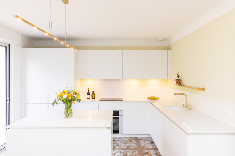 Modern inredning av ett stort vit vitt kök, med en undermonterad diskho, släta luckor, vita skåp, bänkskiva i kvartsit, vitt stänkskydd, integrerade vitvaror, terrazzogolv, en köksö och brunt golv