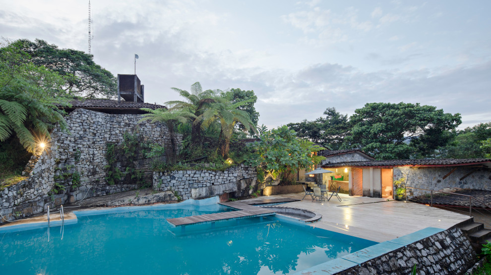 Modelo de piscina natural rústica grande a medida en patio trasero con paisajismo de piscina y losas de hormigón
