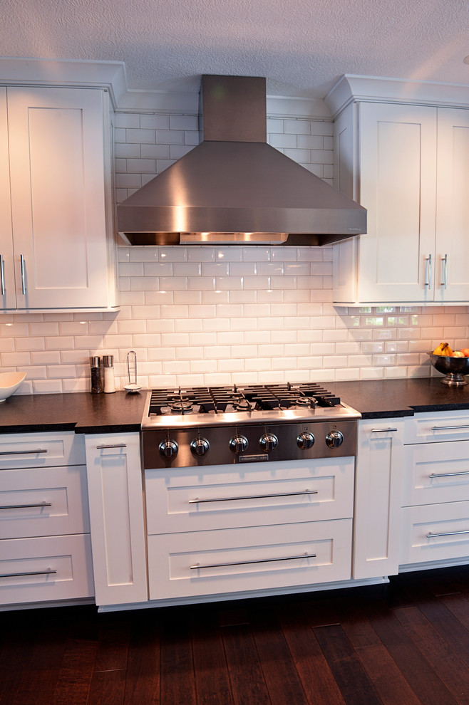 Example of a transitional dark wood floor kitchen design in Cleveland with a drop-in sink, recessed-panel cabinets, white backsplash, ceramic backsplash, stainless steel appliances and an island