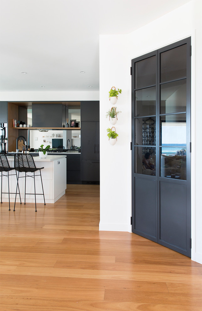 Photo of a large contemporary galley eat-in kitchen in Gold Coast - Tweed with a drop-in sink, flat-panel cabinets, light wood cabinets, quartz benchtops, mirror splashback, black appliances, light hardwood floors, with island and brown floor.
