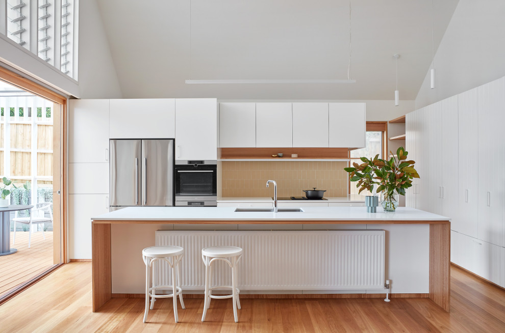 Large contemporary l-shaped eat-in kitchen in Melbourne with a double-bowl sink, flat-panel cabinets, white cabinets, quartz benchtops, white splashback, matchstick tile splashback, stainless steel appliances, medium hardwood floors, with island, brown floor and white benchtop.