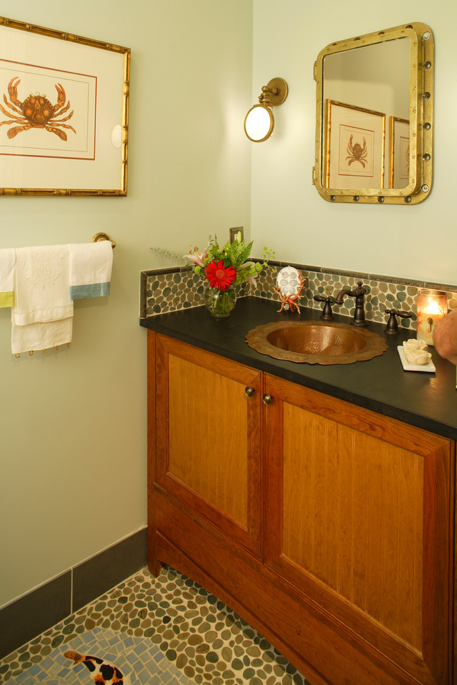 This is an example of a small beach style powder room in Philadelphia with a drop-in sink, recessed-panel cabinets, medium wood cabinets, pebble tile, green walls and black benchtops.