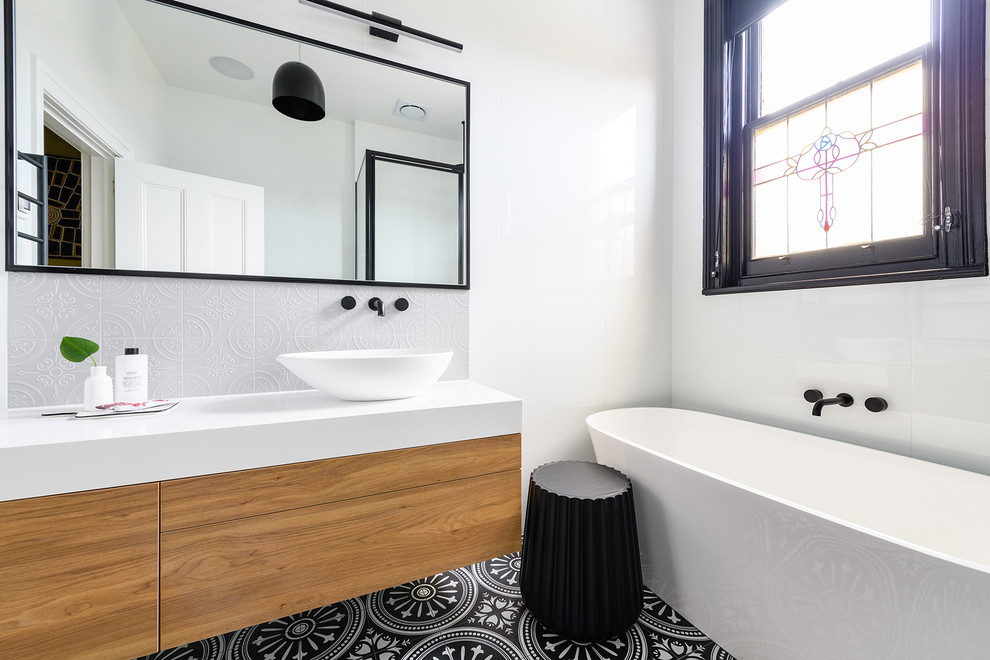 Inspiration for a contemporary bathroom in Hobart with flat-panel cabinets, medium wood cabinets, a freestanding tub, white tile, white walls, a vessel sink, multi-coloured floor and white benchtops.