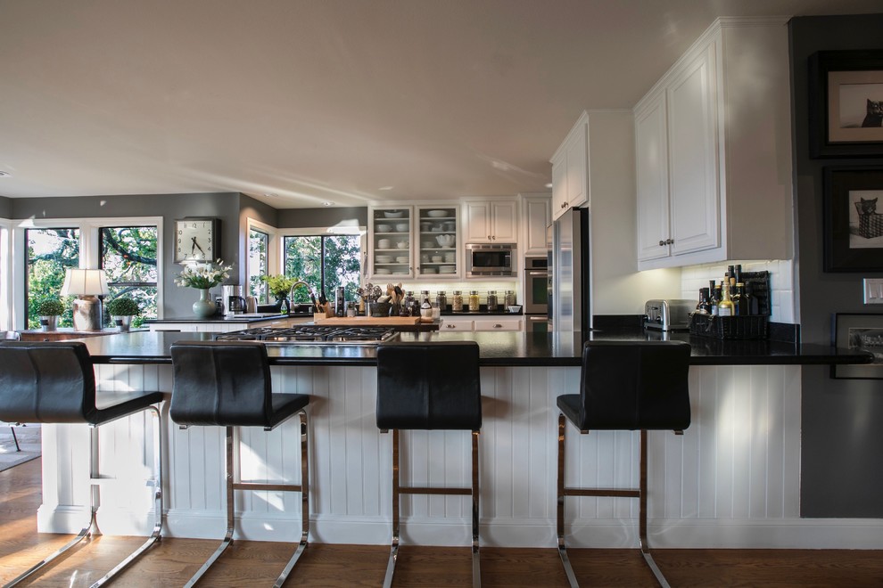 Inspiration for a large contemporary u-shaped open plan kitchen in San Francisco with an undermount sink, glass-front cabinets, white cabinets, granite benchtops, white splashback, subway tile splashback, stainless steel appliances, multiple islands and black benchtop.