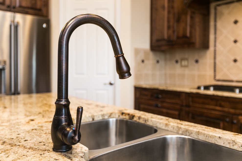 Inspiration for a large rustic l-shaped ceramic tile and multicolored floor eat-in kitchen remodel in Albuquerque with dark wood cabinets, granite countertops, beige backsplash, stone tile backsplash, stainless steel appliances, an island, a double-bowl sink and raised-panel cabinets