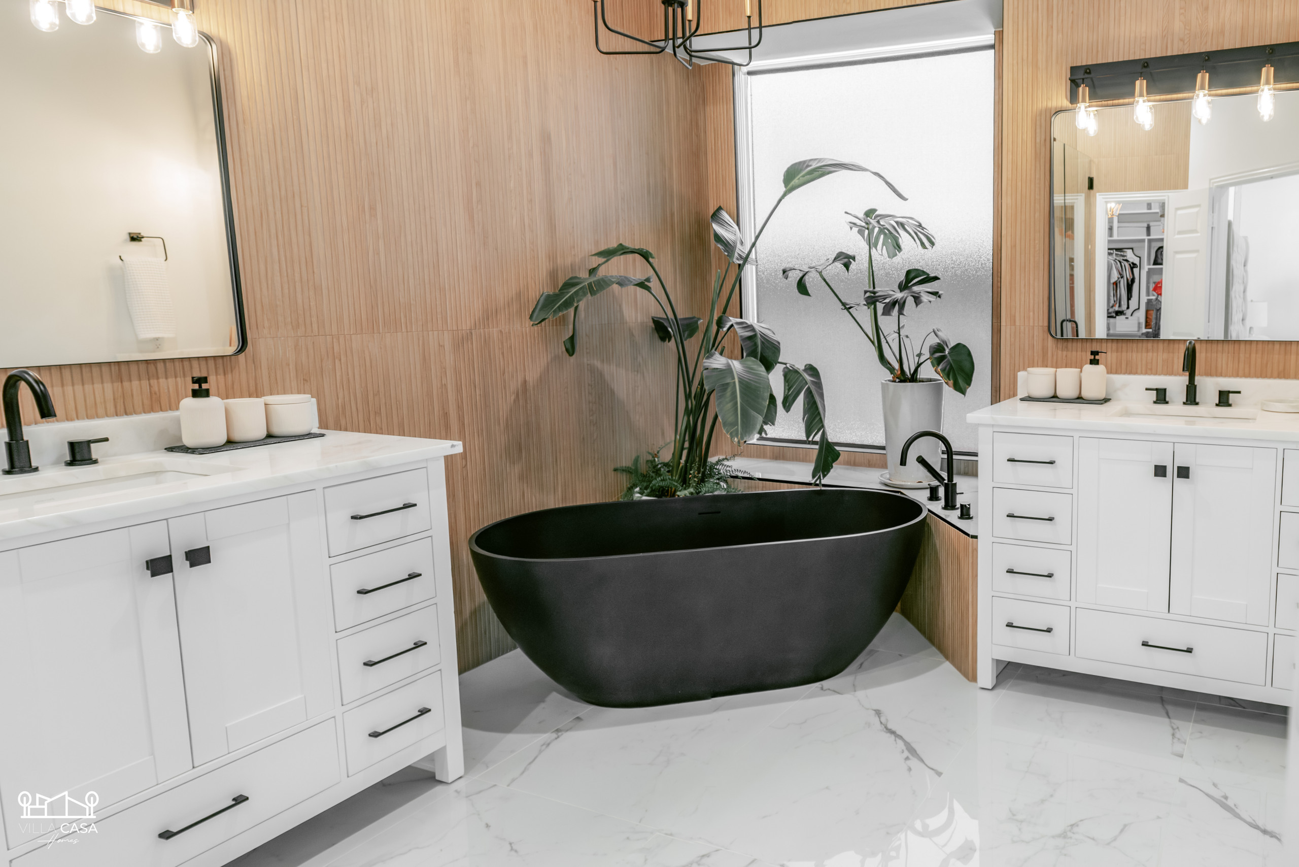 Primary bath remodel featuring new flooring, wall wood look ribbon tile, mirrors, lighting fixtures, vanity, marble countertop, shower tile, glass shower enclosure, and tub.