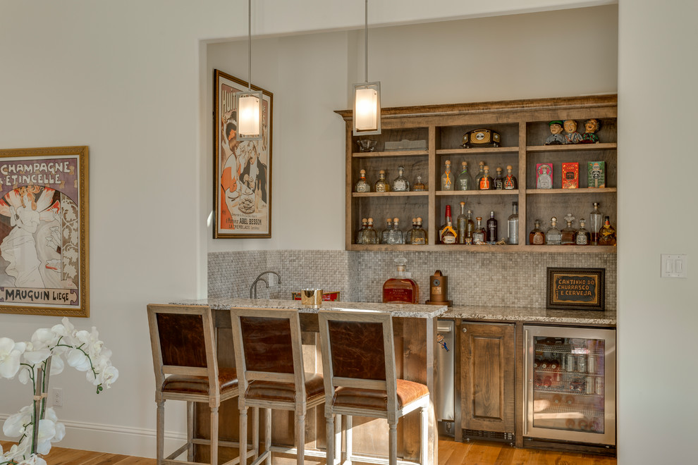 This is an example of a transitional galley seated home bar in Dallas with raised-panel cabinets, beige splashback and mosaic tile splashback.
