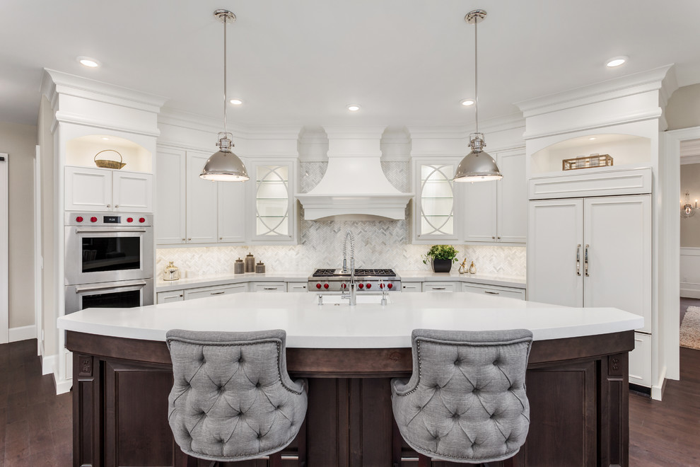 Photo of a transitional u-shaped kitchen in DC Metro with an undermount sink, beaded inset cabinets, white cabinets, grey splashback, panelled appliances, dark hardwood floors, with island, brown floor and white benchtop.