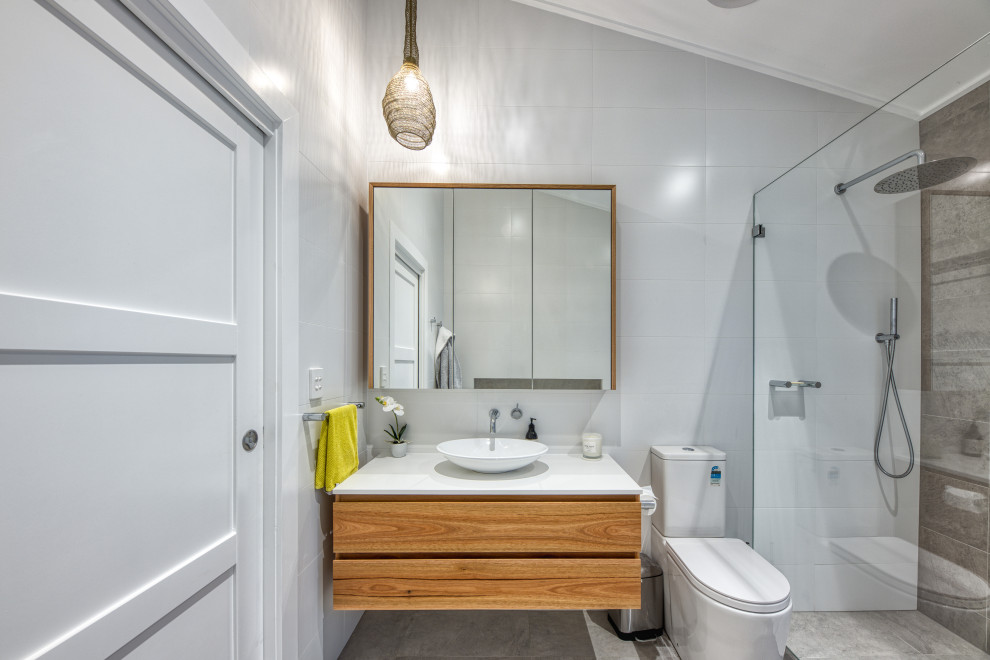 This is an example of a mid-sized beach style 3/4 bathroom in Sydney with flat-panel cabinets, medium wood cabinets, an alcove shower, a one-piece toilet, gray tile, porcelain tile, a vessel sink, grey floor, white benchtops, a single vanity and a freestanding vanity.