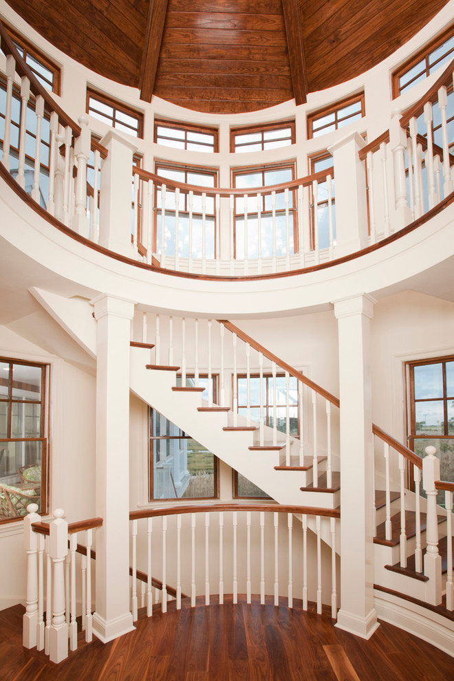 Photo of a large beach style wood curved staircase in Other with painted wood risers and wood railing.