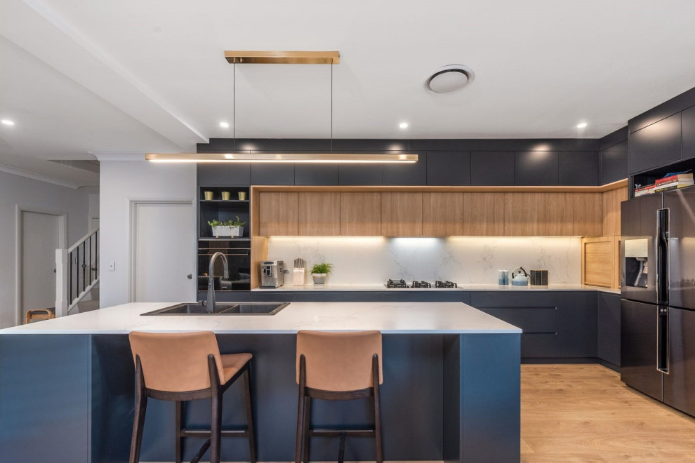 Mid-sized modern l-shaped open plan kitchen in Sydney with a double-bowl sink, recessed-panel cabinets, blue cabinets, marble benchtops, white splashback, marble splashback, black appliances, medium hardwood floors, with island and white benchtop.