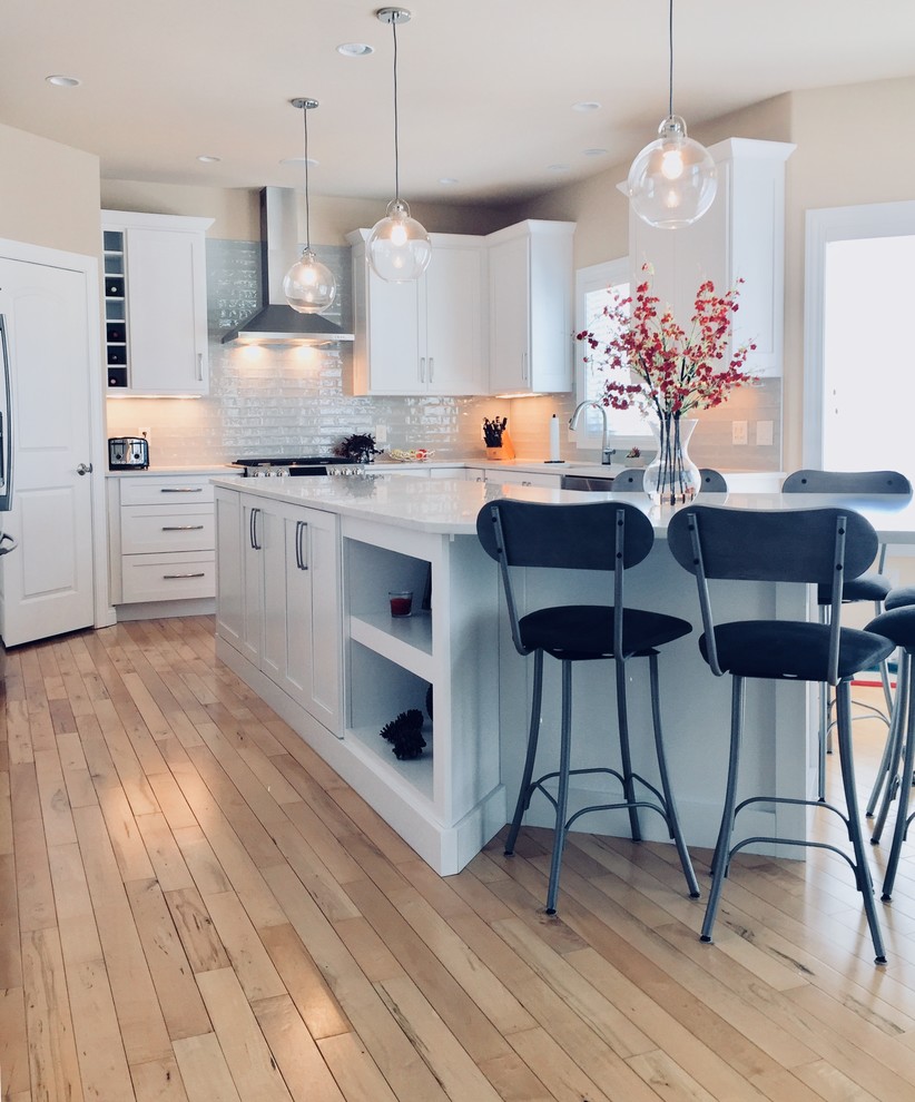 Inspiration for a transitional light wood floor kitchen remodel with an undermount sink, shaker cabinets, white cabinets, quartz countertops, blue backsplash, glass tile backsplash, stainless steel appliances and an island