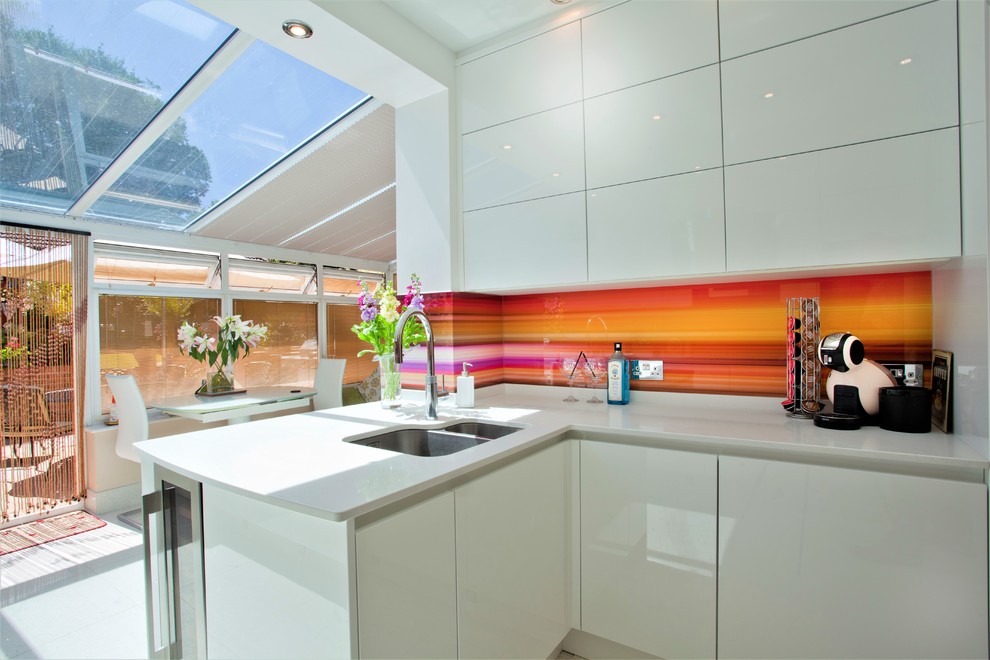 Inspiration for a contemporary l-shaped eat-in kitchen in Hampshire with a double-bowl sink, flat-panel cabinets, white cabinets, multi-coloured splashback, glass sheet splashback, a peninsula, grey floor and white benchtop.