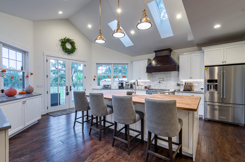 This is an example of a large country u-shaped eat-in kitchen in Chicago with a double-bowl sink, raised-panel cabinets, white cabinets, wood benchtops, white splashback, ceramic splashback, stainless steel appliances, bamboo floors, with island, brown floor, brown benchtop and vaulted.