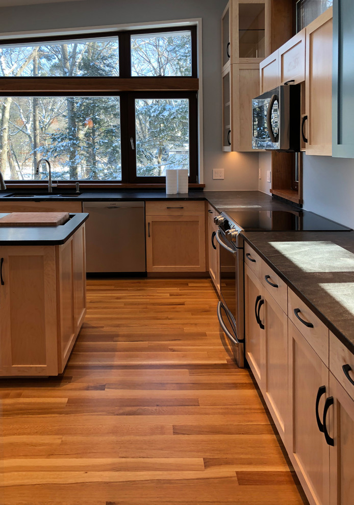 Photo of a large modern l-shaped eat-in kitchen in Boston with an undermount sink, shaker cabinets, light wood cabinets, soapstone benchtops, stainless steel appliances, medium hardwood floors, with island, multi-coloured floor and grey benchtop.