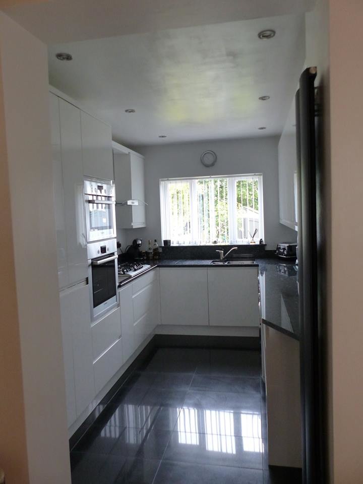 This is an example of a contemporary galley kitchen in West Midlands with white cabinets and granite benchtops.