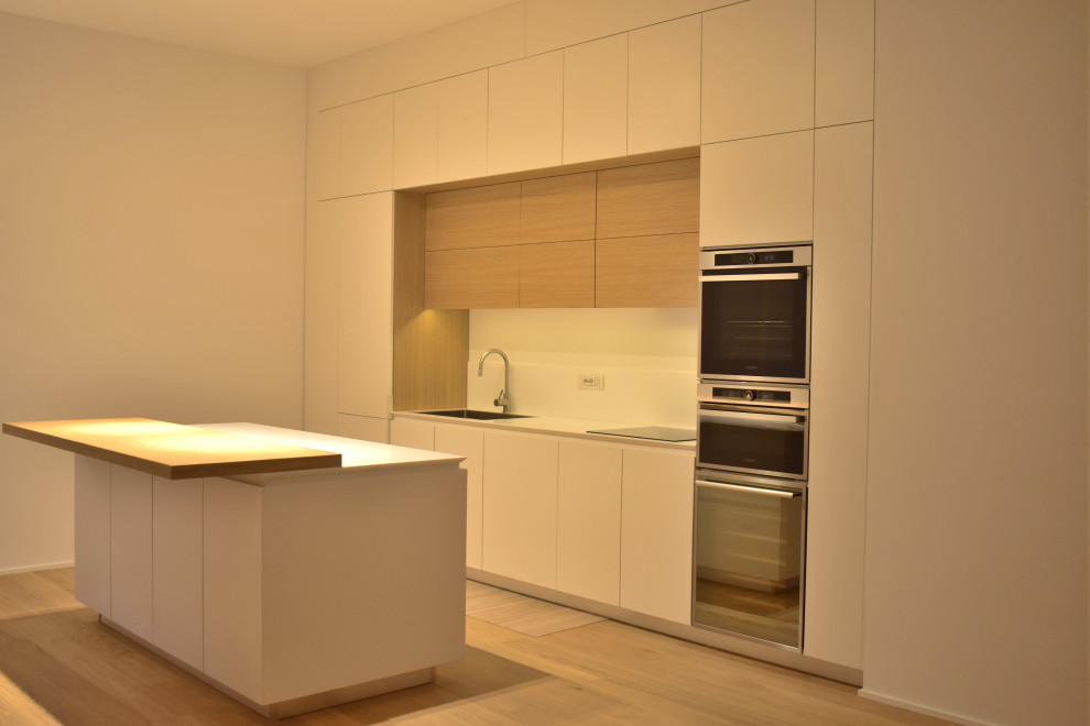 Design ideas for a mid-sized modern single-wall open plan kitchen in Milan with a drop-in sink, beaded inset cabinets, white cabinets, solid surface benchtops, white splashback, stainless steel appliances, painted wood floors, with island and white benchtop.
