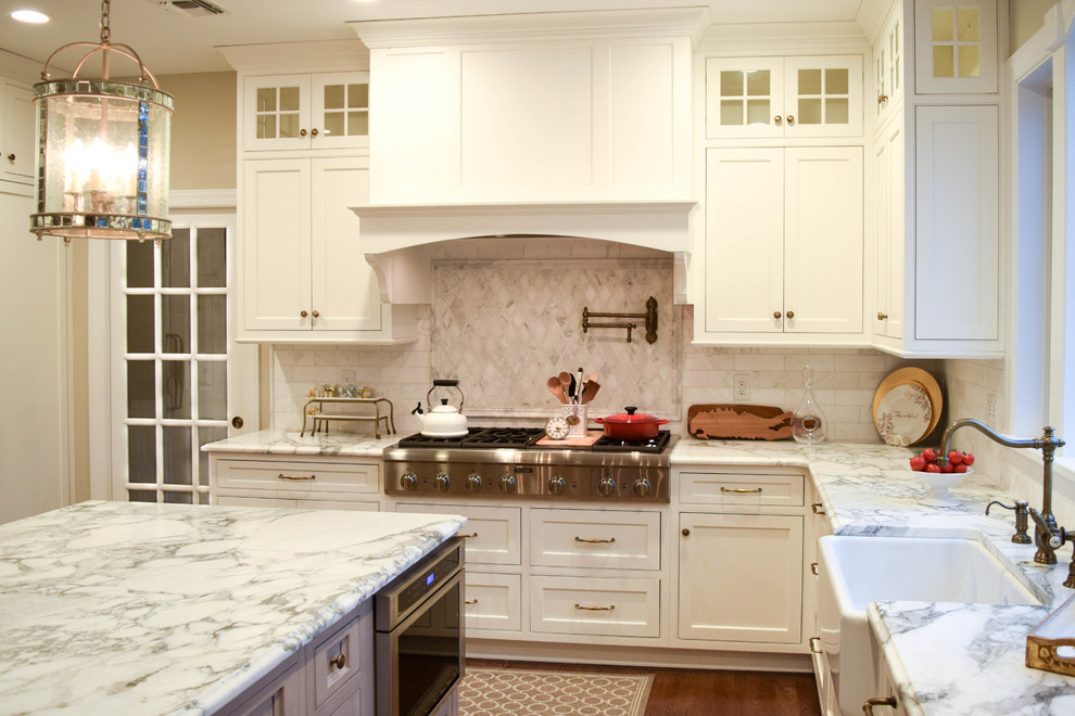 This is an example of an expansive traditional l-shaped eat-in kitchen in New York with a farmhouse sink, beaded inset cabinets, white cabinets, marble benchtops, white splashback, stone tile splashback, panelled appliances, medium hardwood floors and with island.