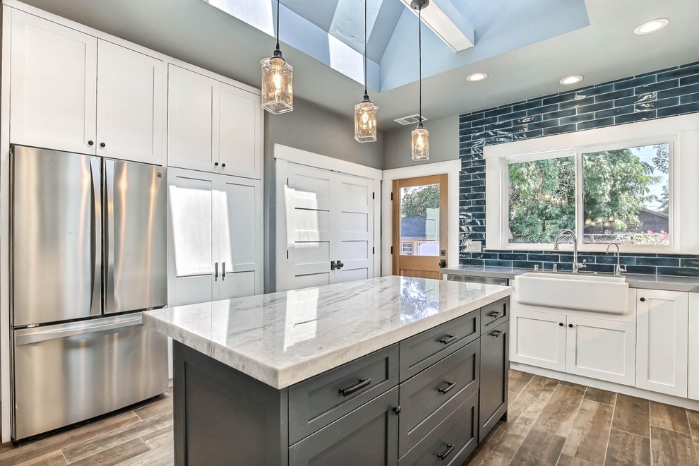 Example of a mid-sized transitional u-shaped medium tone wood floor and brown floor eat-in kitchen design in San Francisco with a farmhouse sink, shaker cabinets, white cabinets, quartzite countertops, blue backsplash, porcelain backsplash, stainless steel appliances, an island and gray countertops
