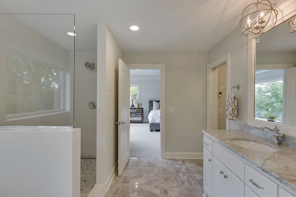 This is an example of a large traditional master bathroom in Minneapolis with recessed-panel cabinets, white cabinets, a freestanding tub, an open shower, a two-piece toilet, white tile, subway tile, white walls, porcelain floors, an undermount sink, marble benchtops, grey floor and an open shower.