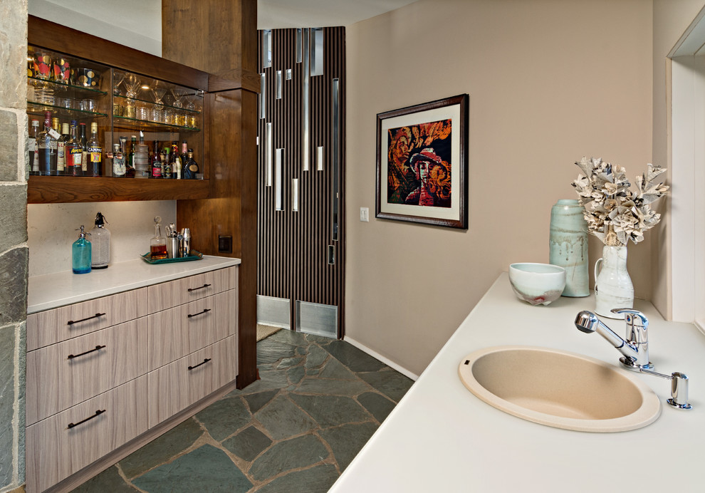 Photo of a large contemporary galley wet bar in Minneapolis with a drop-in sink, flat-panel cabinets, beige cabinets, glass benchtops, beige splashback, limestone splashback, slate floors and turquoise floor.