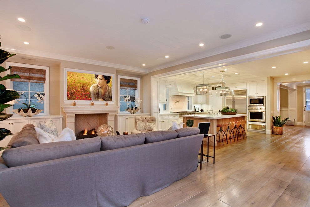 Photo of a beach style open concept family room in Orange County with beige walls, medium hardwood floors, a standard fireplace, a stone fireplace surround, a wall-mounted tv and beige floor.