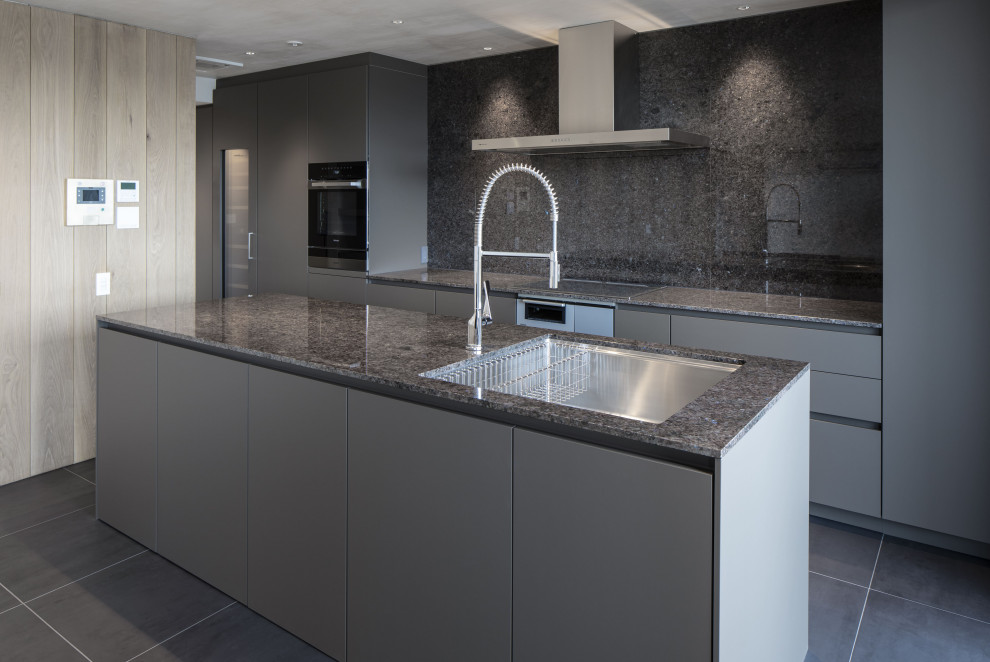 Mid-sized modern single-wall open plan kitchen in Nagoya with an undermount sink, beaded inset cabinets, grey cabinets, granite benchtops, grey splashback, granite splashback, black appliances, ceramic floors, with island, black floor, grey benchtop and timber.