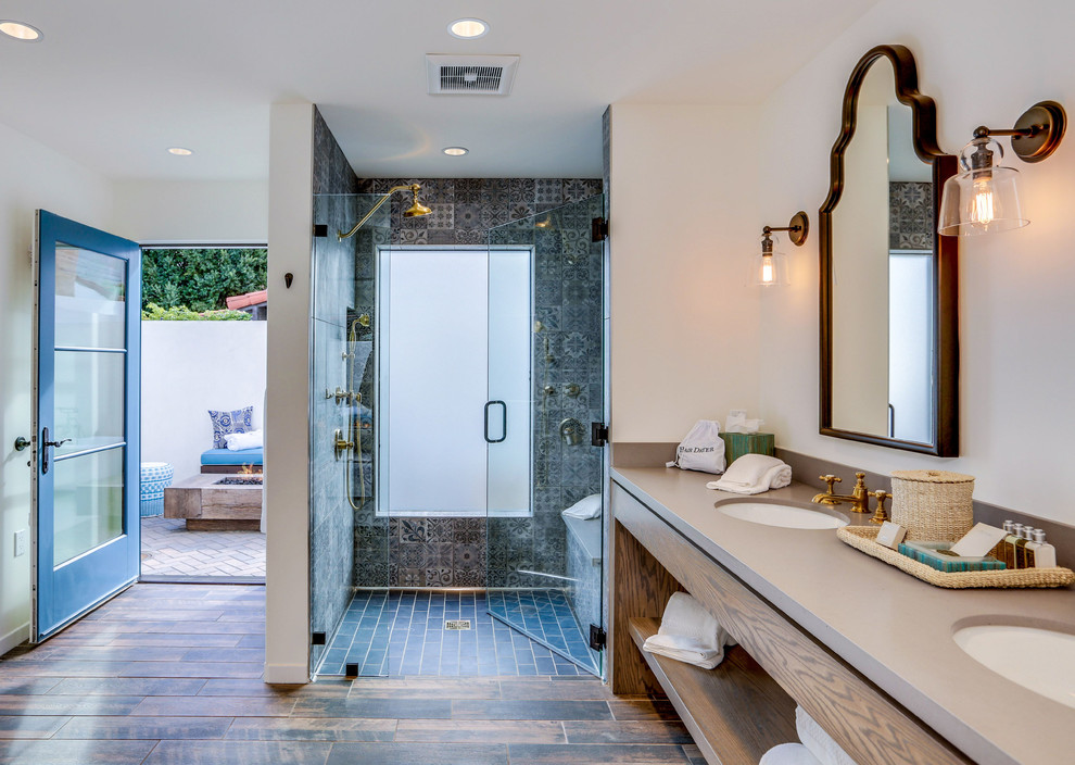 Inspiration for a mediterranean master bathroom in Los Angeles with flat-panel cabinets, medium wood cabinets, an alcove shower, blue tile, gray tile, white walls, dark hardwood floors, an undermount sink, brown floor, a hinged shower door and brown benchtops.