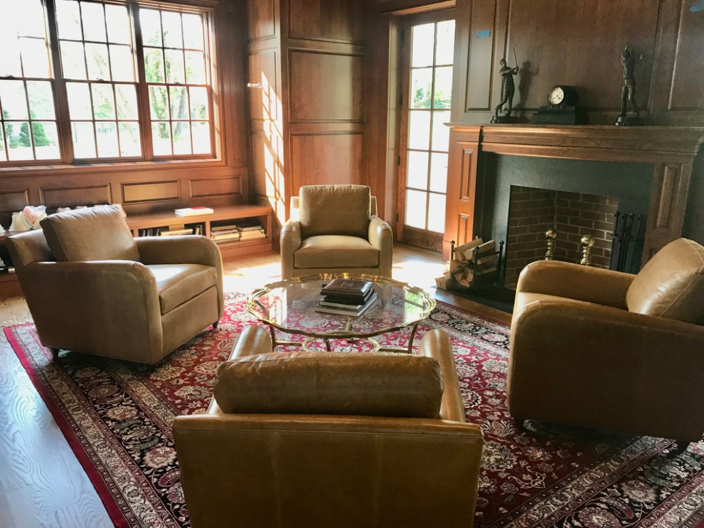 Photo of a large traditional enclosed living room in Philadelphia with a library, brown walls, medium hardwood floors, a standard fireplace, a stone fireplace surround, no tv, brown floor, coffered and panelled walls.