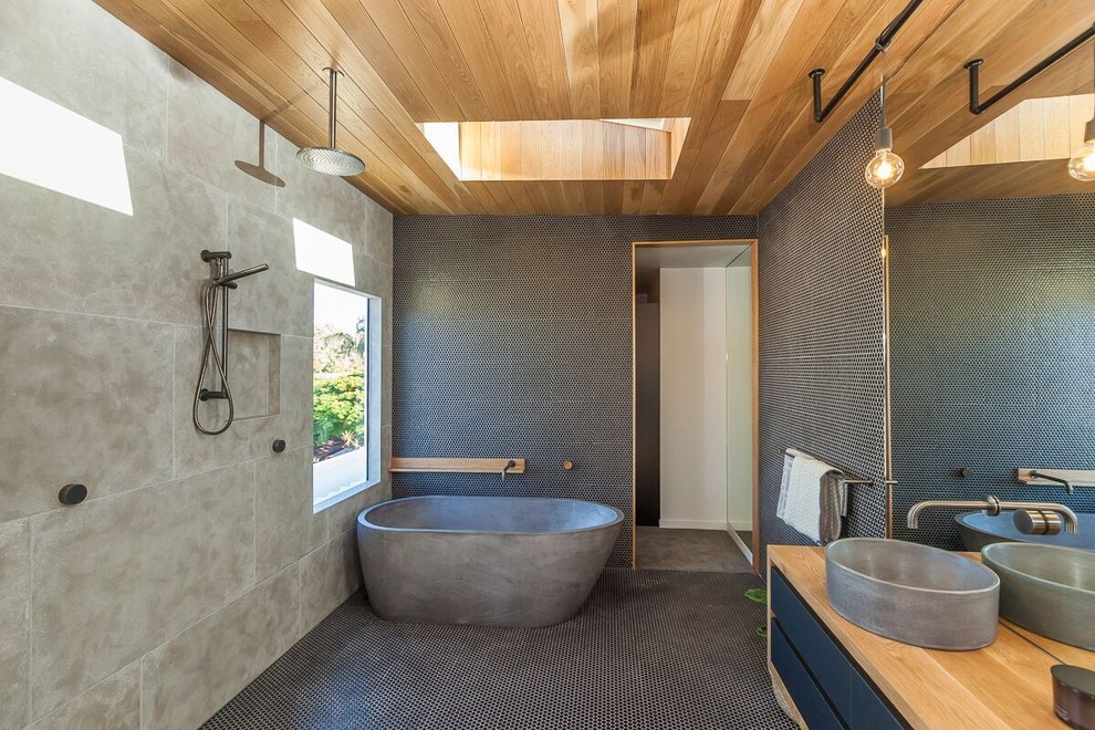 This is an example of a contemporary master wet room bathroom in Gold Coast - Tweed with flat-panel cabinets, black cabinets, a freestanding tub, black tile, gray tile, mosaic tile, mosaic tile floors, a vessel sink, wood benchtops, black floor and an open shower.