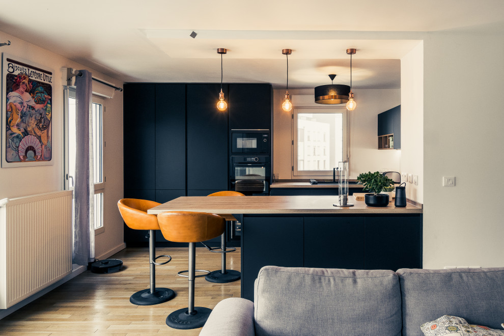 Design ideas for a mid-sized modern u-shaped open plan kitchen in Paris with black cabinets, wood benchtops, black appliances and with island.
