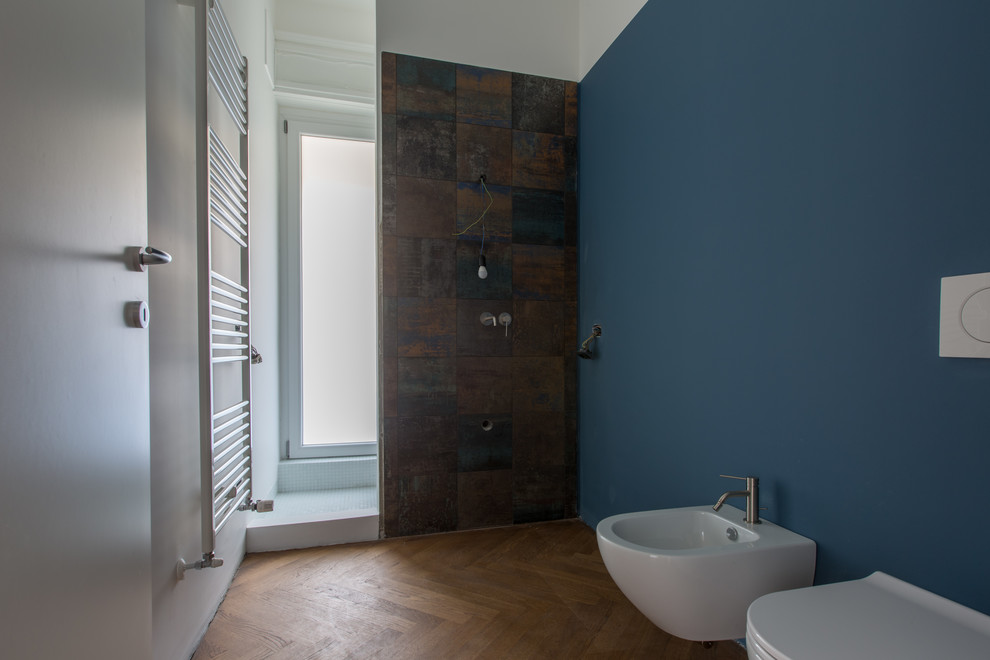 Small contemporary master bathroom in Milan with grey cabinets, a curbless shower, a wall-mount toilet, multi-coloured tile, porcelain tile, blue walls, light hardwood floors, a vessel sink, glass benchtops, an open shower and grey benchtops.