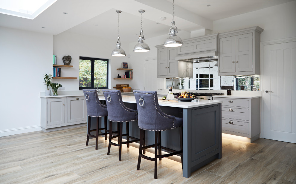 This is an example of a large transitional l-shaped kitchen in Hertfordshire with shaker cabinets, grey cabinets, mirror splashback, with island, beige floor and white benchtop.