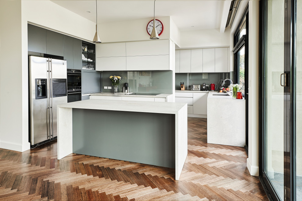 Photo of a mid-sized contemporary l-shaped open plan kitchen in Melbourne with an undermount sink, white cabinets, quartz benchtops, grey splashback, stainless steel appliances, medium hardwood floors, with island, brown floor, flat-panel cabinets, glass sheet splashback and white benchtop.