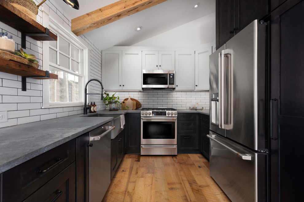 Inspiration for a small country u-shaped eat-in kitchen with a farmhouse sink, shaker cabinets, black cabinets, concrete benchtops, white splashback, ceramic splashback, stainless steel appliances, medium hardwood floors, no island, brown floor and grey benchtop.
