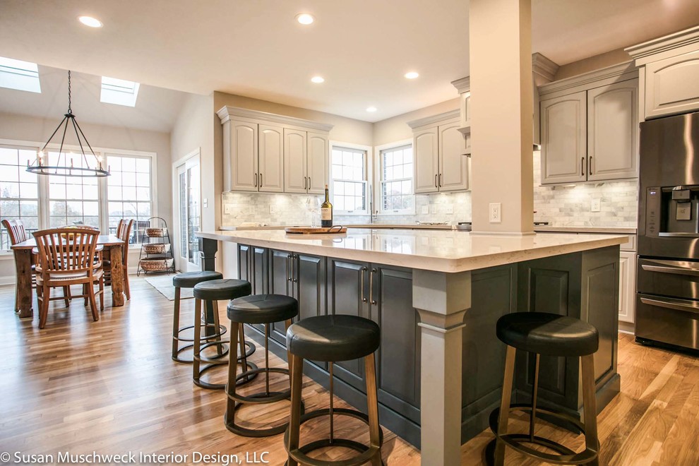 Inspiration for a large transitional l-shaped light wood floor eat-in kitchen remodel with an undermount sink, raised-panel cabinets, gray cabinets, quartz countertops, marble backsplash, stainless steel appliances, an island and white countertops