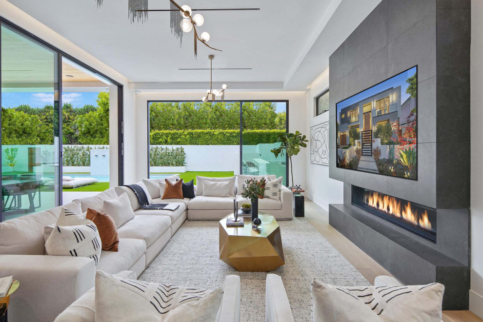 Design ideas for a large contemporary open plan games room in San Francisco with white walls, light hardwood flooring, a standard fireplace, a tiled fireplace surround, a wall mounted tv and brown floors.