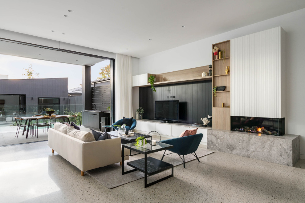 Diseño de salón abierto contemporáneo de tamaño medio con paredes blancas, suelo de cemento, chimenea de doble cara, marco de chimenea de piedra y suelo gris
