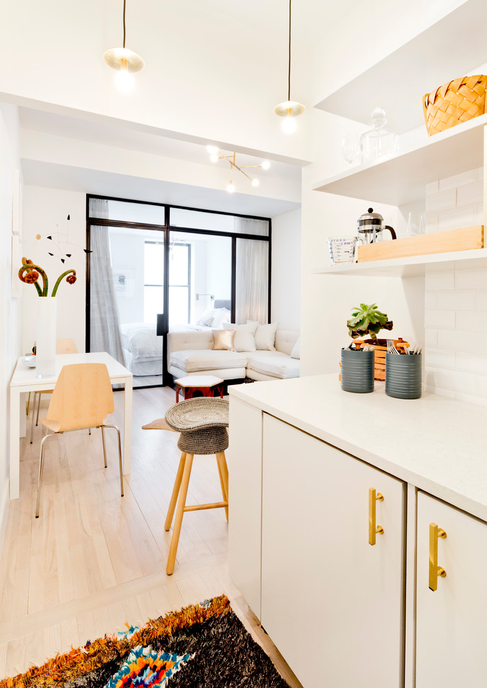 Design ideas for a small contemporary l-shaped open plan kitchen in New York with an undermount sink, open cabinets, white cabinets, quartz benchtops, white splashback, subway tile splashback, panelled appliances, light hardwood floors and no island.